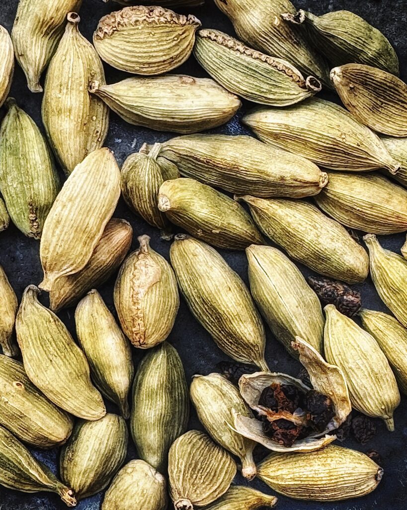 a close up photo of green cardamom pods, some of them cracked open exposing dark seeds