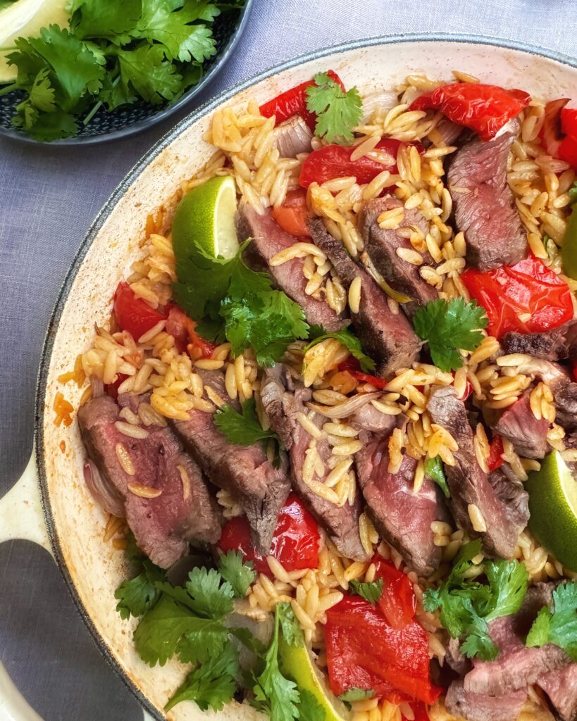 A casserole with Steak and Orzo cooked with Jamaican Jerk, Ginger and Garlic, red bell peppers and coriander leaves