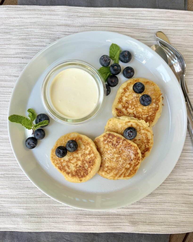 A plate with syrniki, Russian cottage cheese pancakes, served with sour cream and fresh blueberries