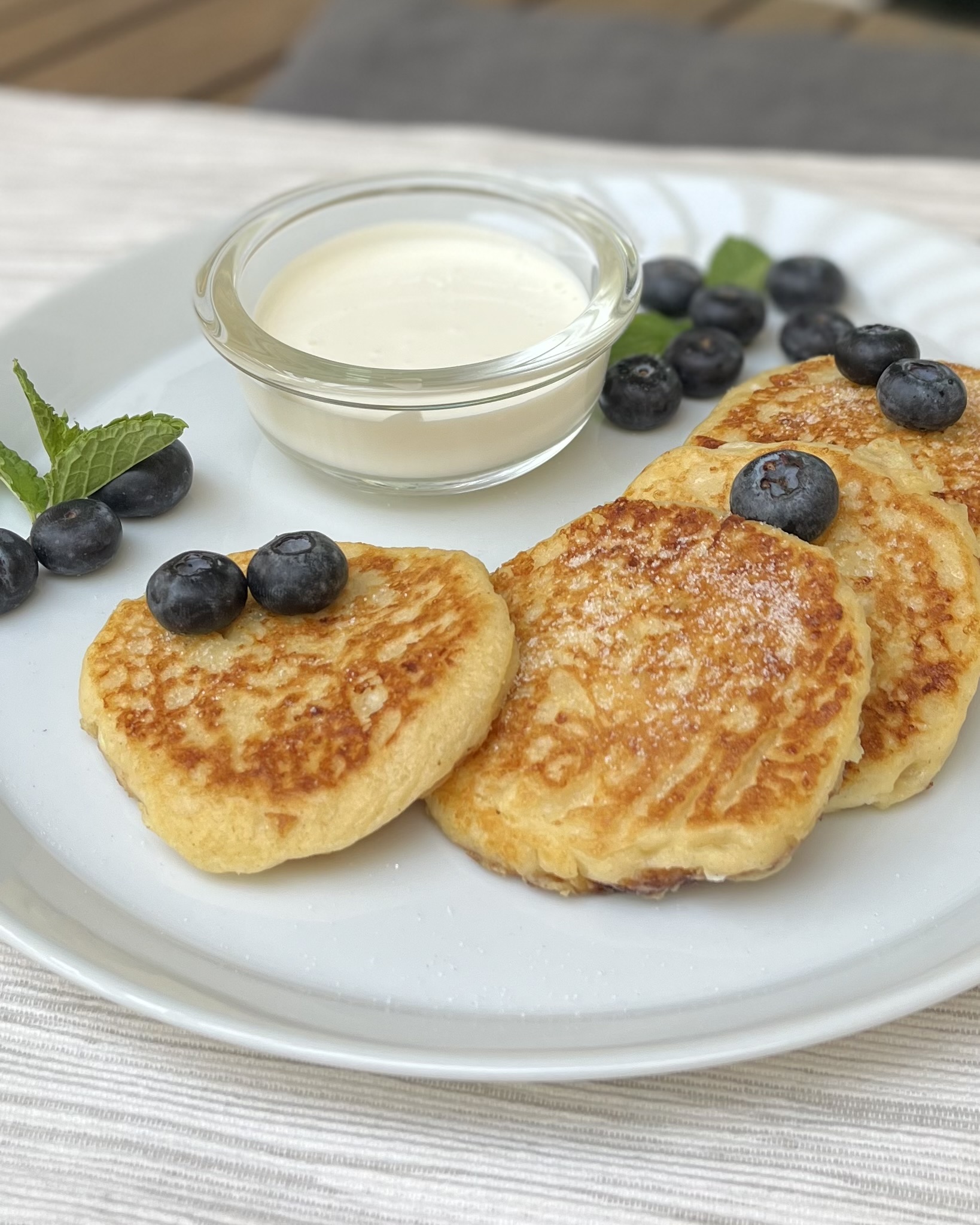 A close up on a plate with syrniki, Russian cottage cheese pancakes, served with sour cream and fresh blueberries