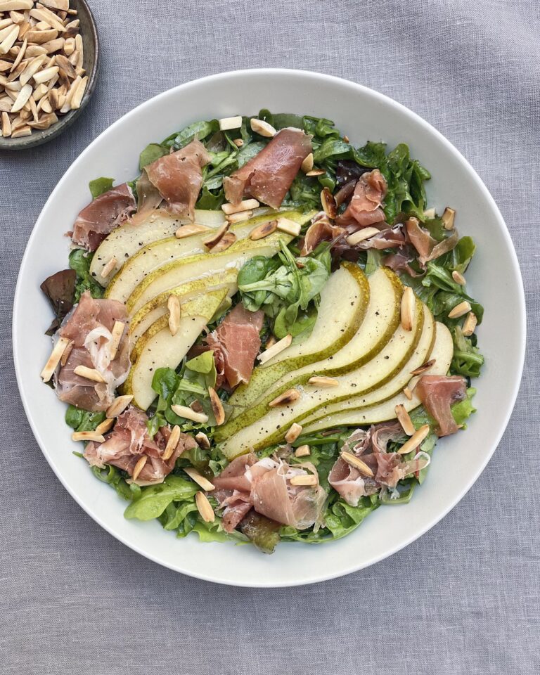 Sliced Conference Pear and slices of Prosciutto over a bed of rocket leaves garnished with roasted almonds