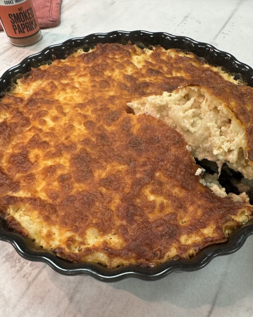 A close up on a round black baking dish with Cauliflower gratin under golden cheese crust