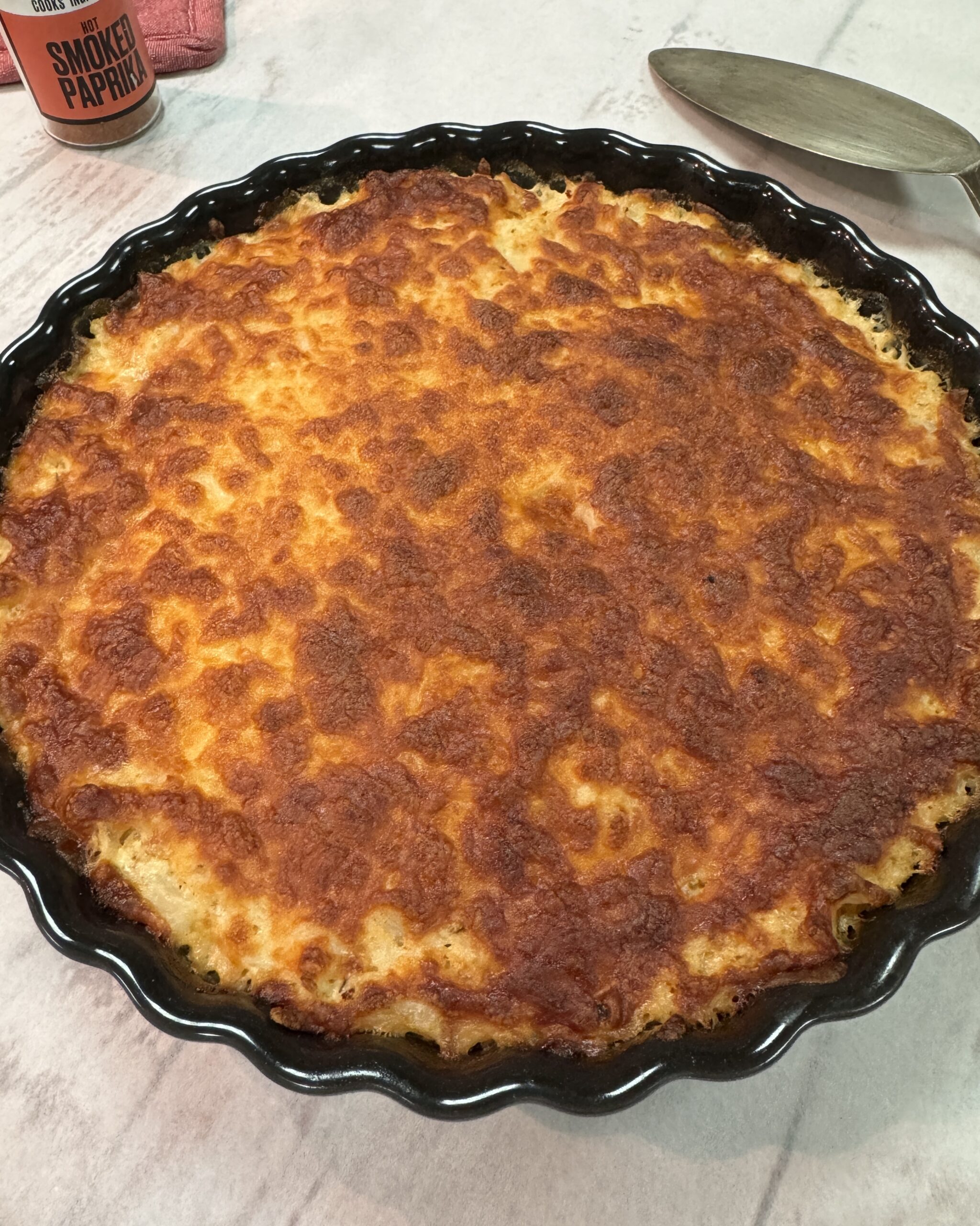 A close up on a round black baking dish with Cauliflower gratin under golden cheese crust