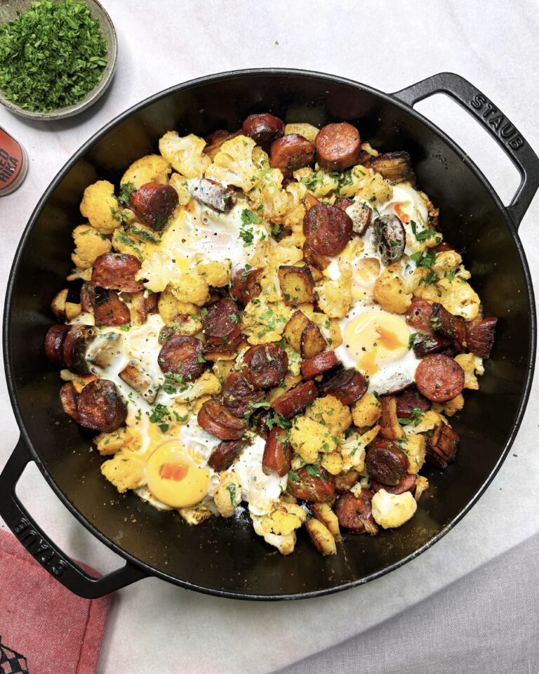 A skillet with fried cauliflower, slices or chorizo and fried egg, garnished with fresh chopped parsley