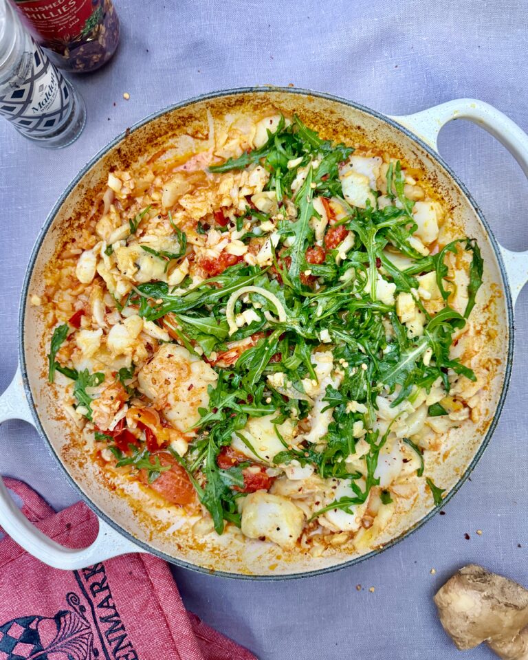 a casserole with chunks of cod, tomatoes and arugula