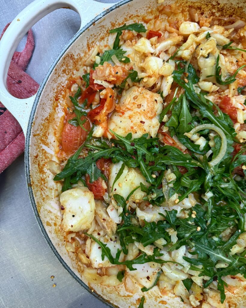 a casserole with chunks of cod, tomatoes and arugula