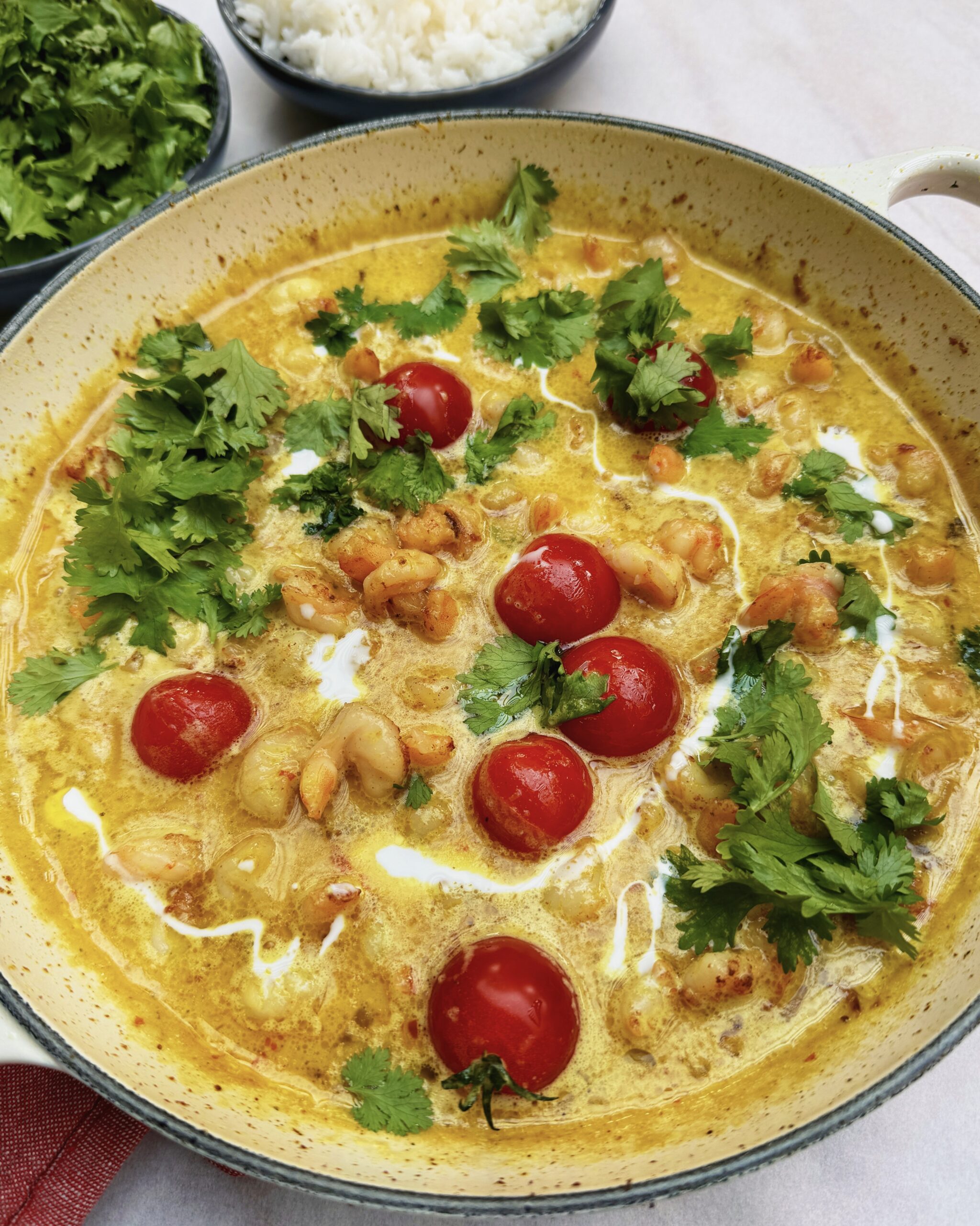 a skillet with yellow coconut curry with shrimps, cherry tomatoes and fresh cilantro