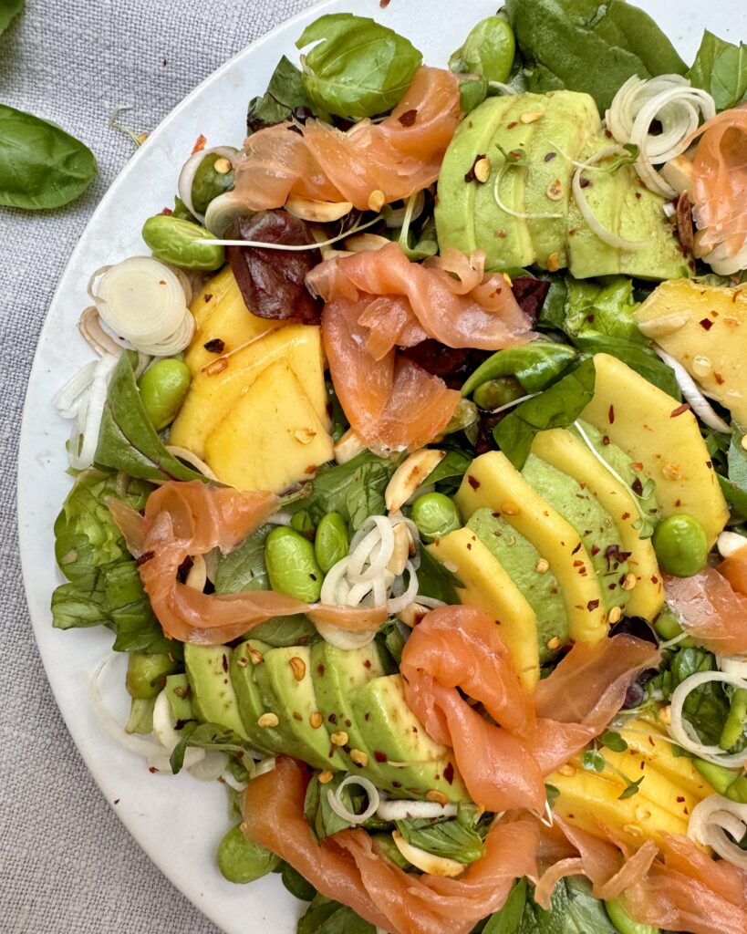 A plate of Smoked Salmon with Mango and Avocado, edamame, leeks and salad greens