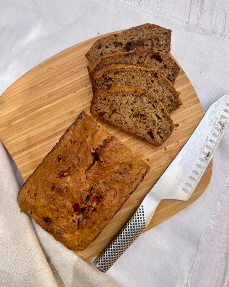 Banana bread on a wooden board with half a loaf intact and the other half sliced