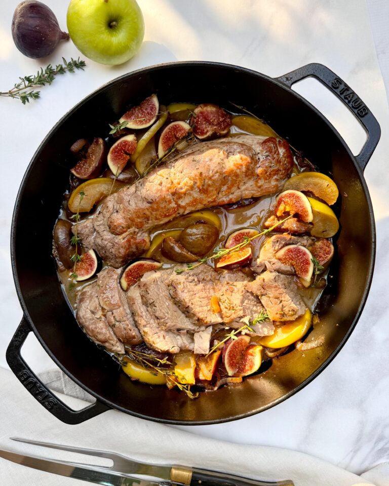 Pork tenderloin in a large black casserole with stewed apples, figs and thyme sprigs