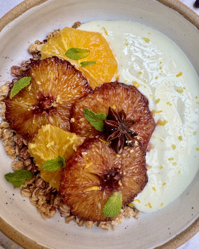 A bowl of granola and yoghurt with red wine syrup topped with fresh and caramelized oranges