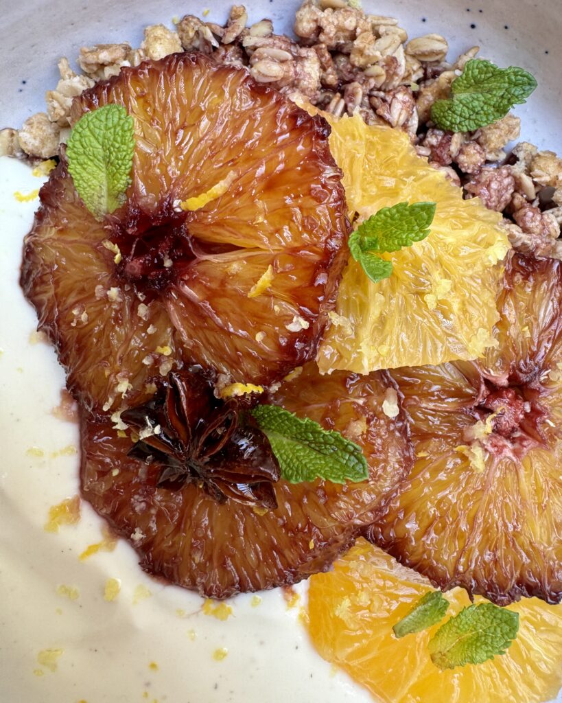 a close up on granola and yoghurt bowl with slices of caramelized orange, mint leaves and lemon zest