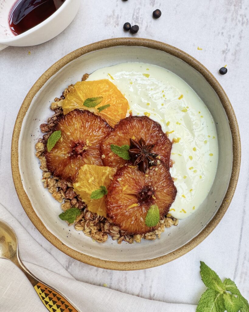 a granola and yoghurt bowl with slices of caramelized orange, mint leaves and lemon zest