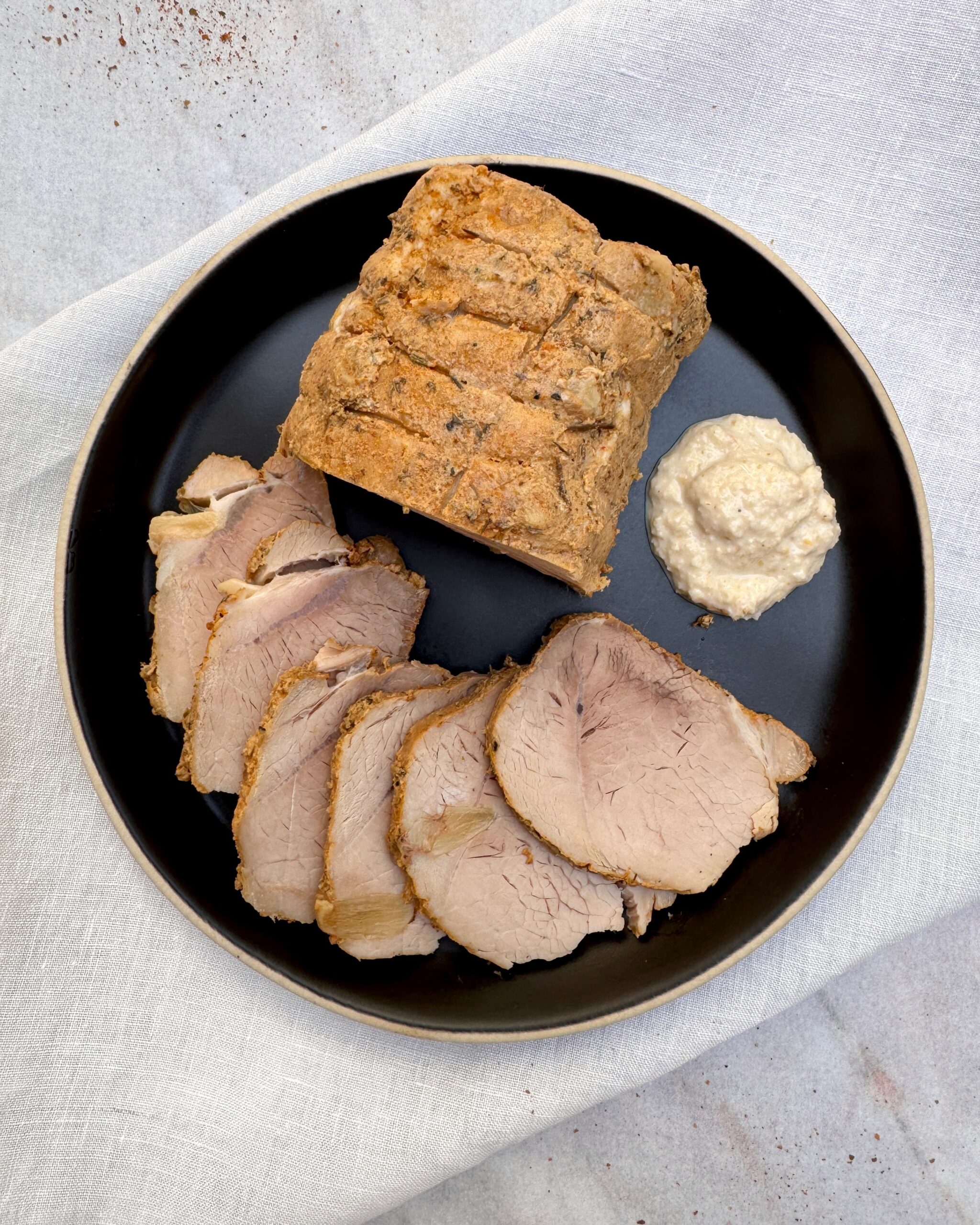 a plate with slices of cold pork roast with garlic, herbs and mustard served with horseradish sauce