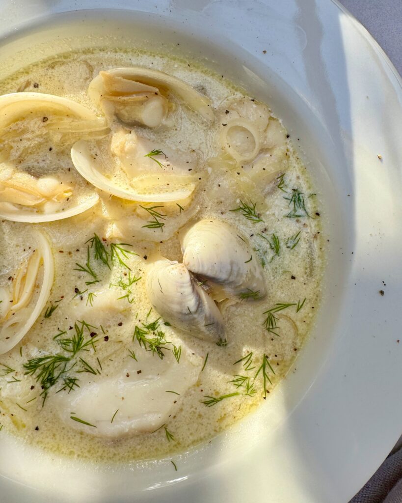 a plate with creamy seafood soup with clams, white fish, leeks, celery, saffron and dill