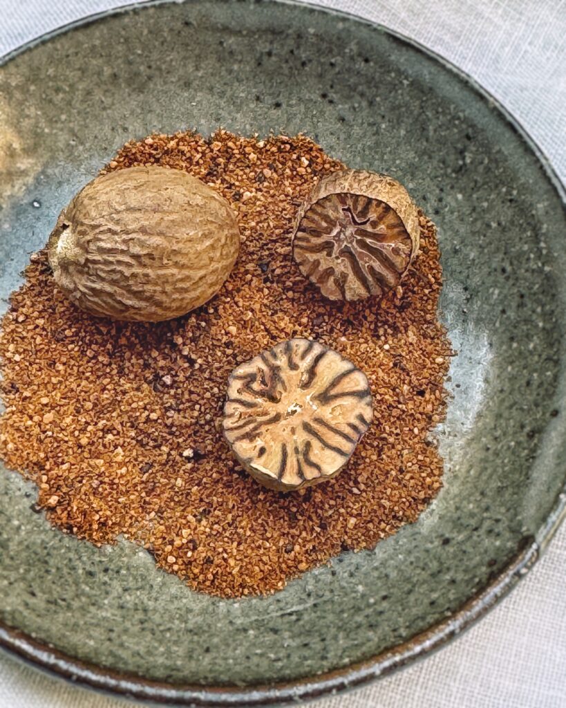 whole nutmeg, half cut nutmeg and freshly ground nutmeg on a plate