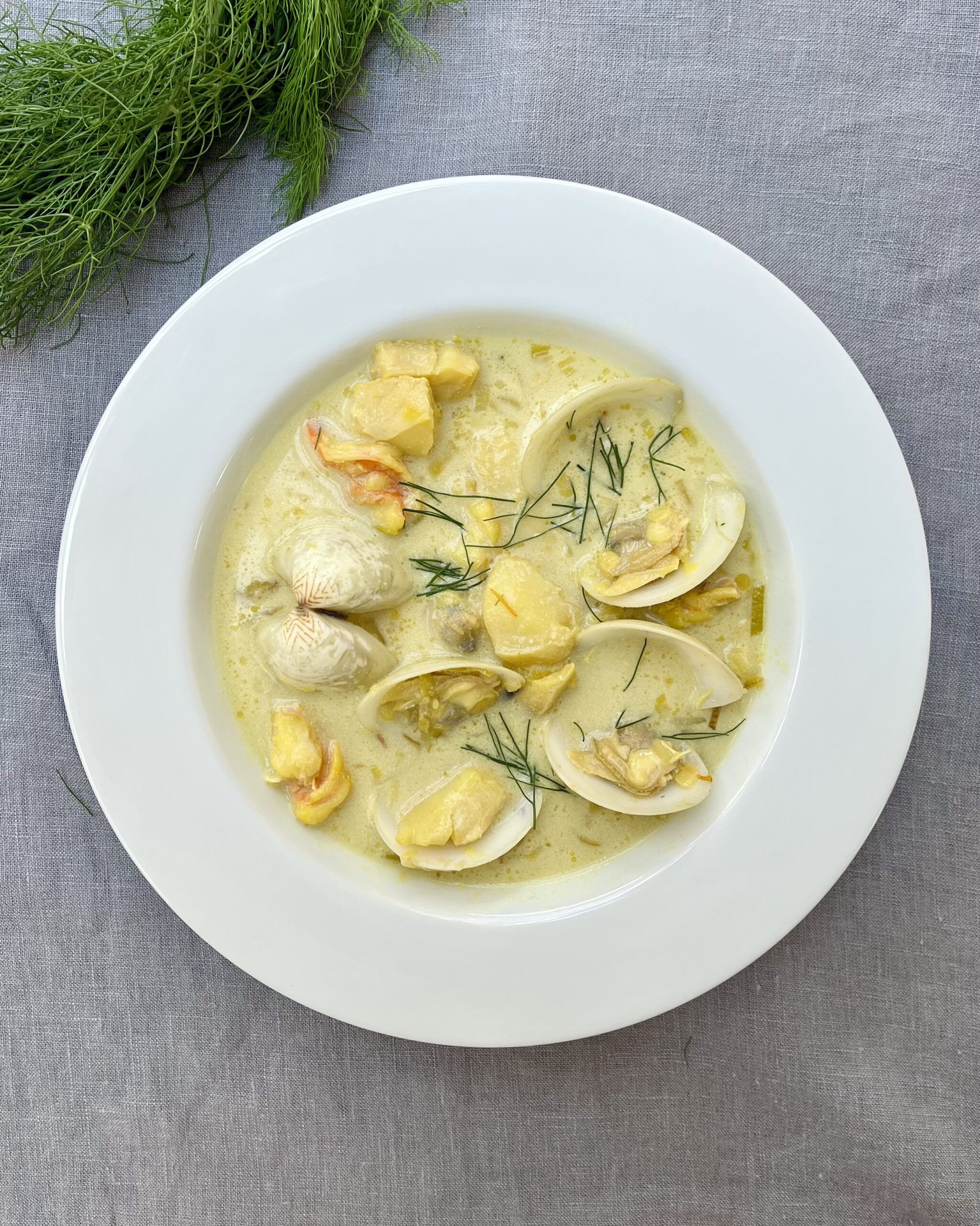 a plate with creamy seafood soup with clams, shrimp, white fish, leeks, celery, saffron and dill