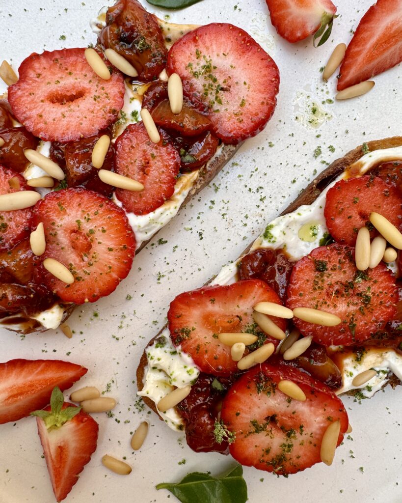 A close up on a plate with sourdough toast with strawberries, ricotta and makrut lime