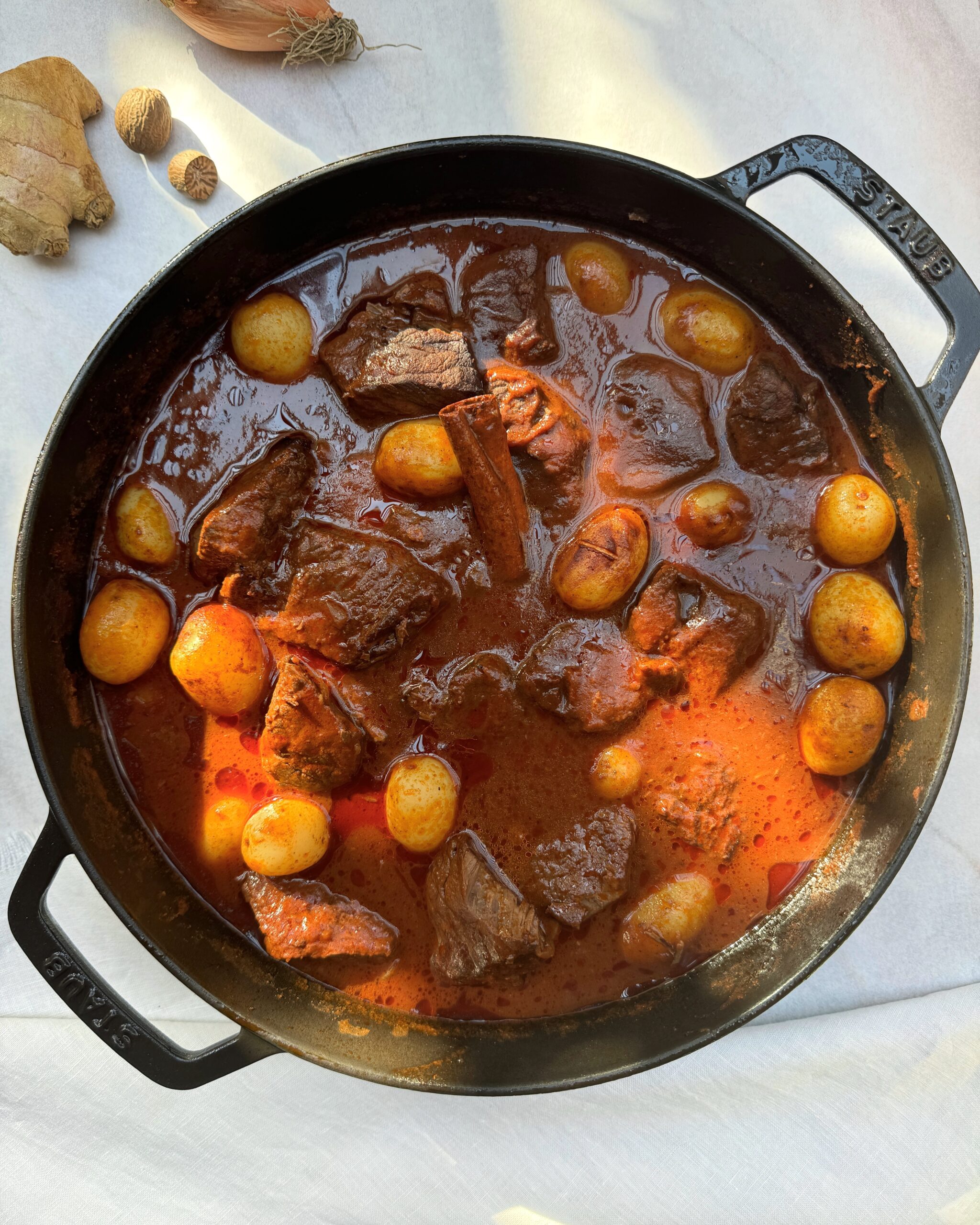 A black casserole with chunks of beef in a rich red sauce with baby potatoes