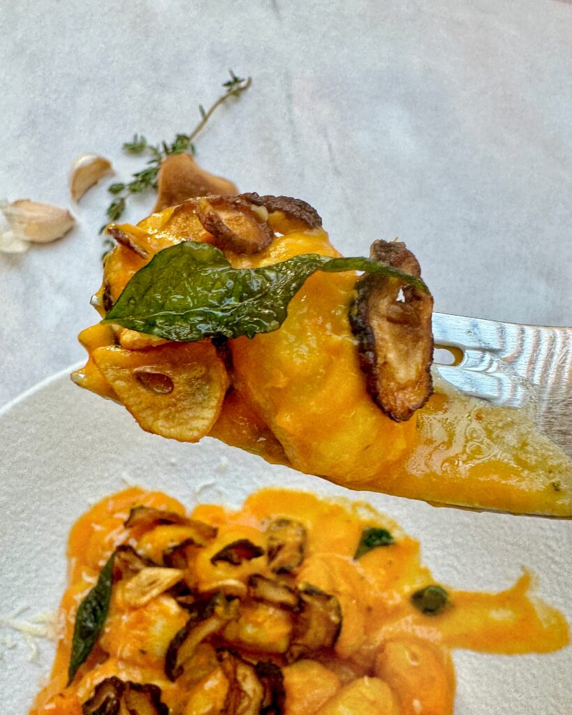 A forkful of Gnocchi in Squash Sauce with fried mushroom caps, garlic chips and crispy curry leaves