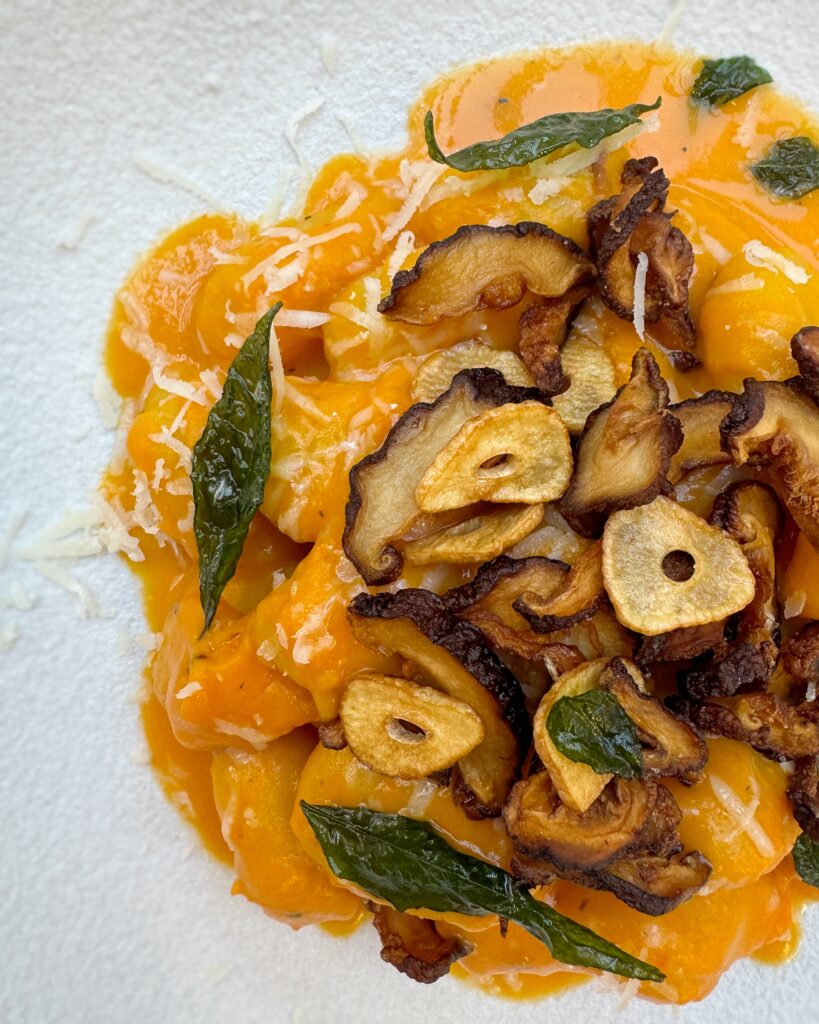 A close up on a plate of Gnocchi in Squash Sauce with fried mushroom caps, garlic chips and crispy curry leaves