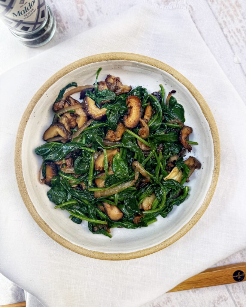 a plate with quick buttery spinach mixed with fried onions, garlic and shiitake mushrooms