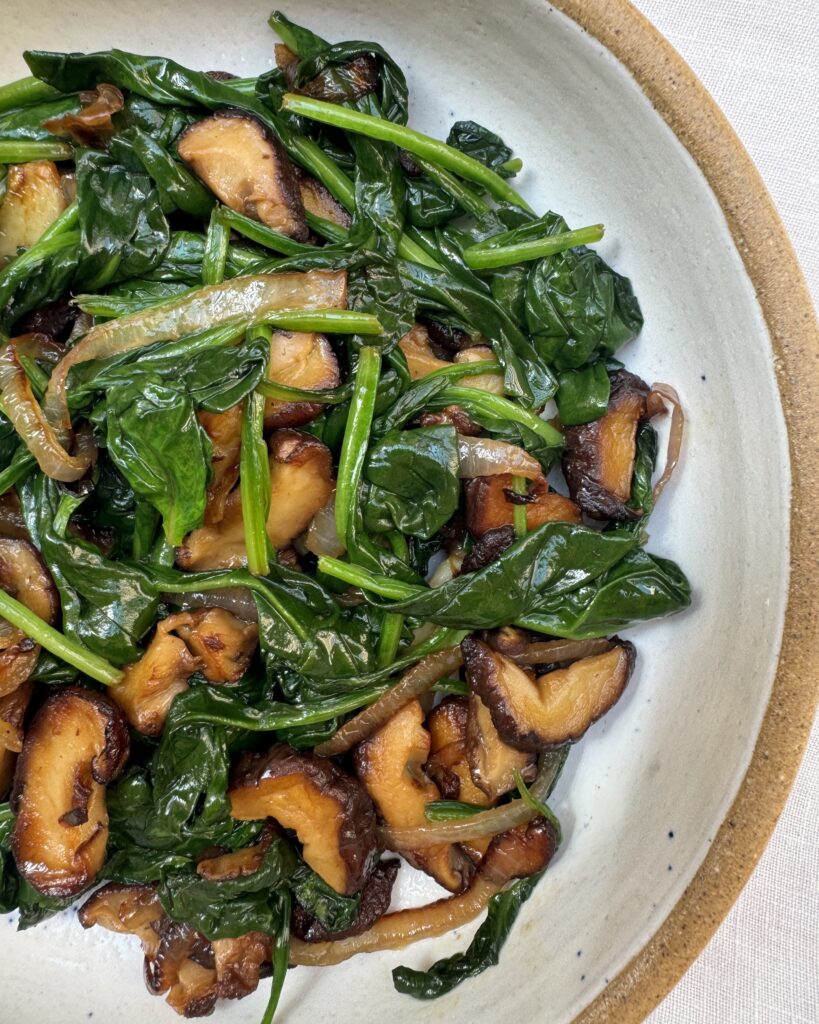 a close up on a plate with quick buttery spinach mixed with fried onions, garlic and shiitake mushrooms