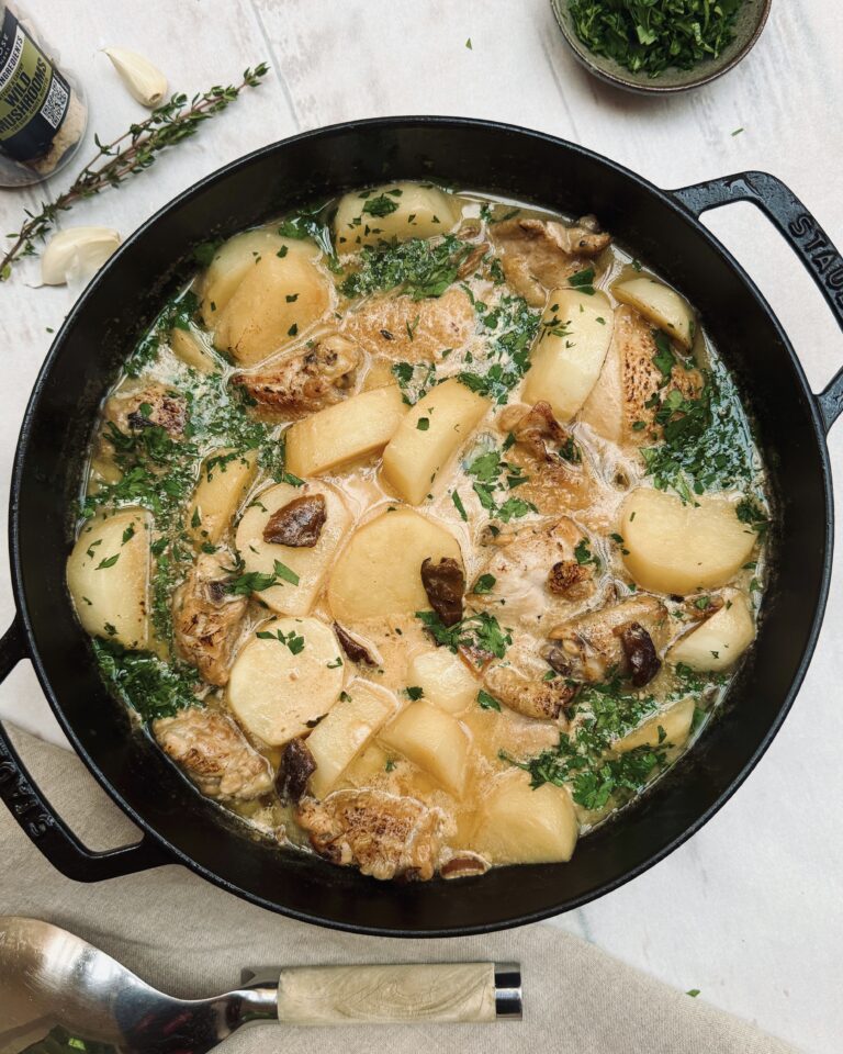 A close up on a casserole with chicken pieces in a creamy sauce with mushrooms, potatoes and fresh parsley