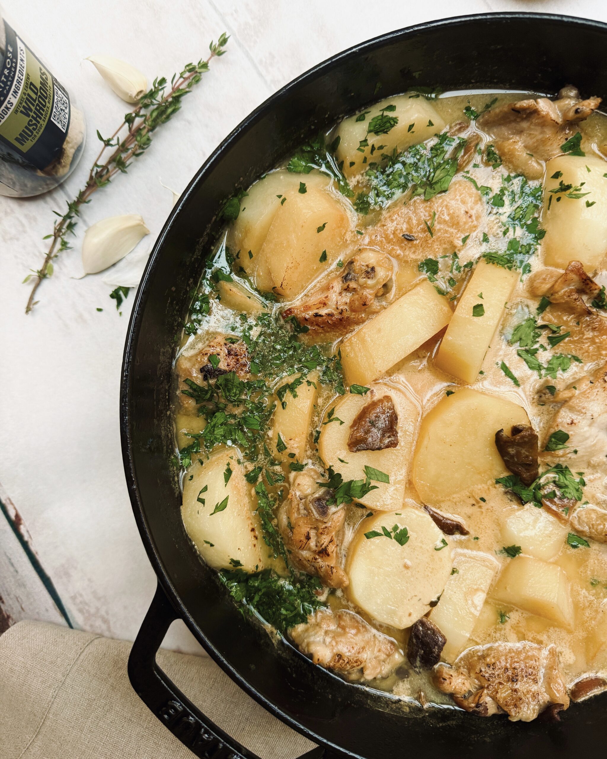 A close up on a casserole with chicken pieces in a creamy sauce with mushrooms, potatoes and fresh parsley