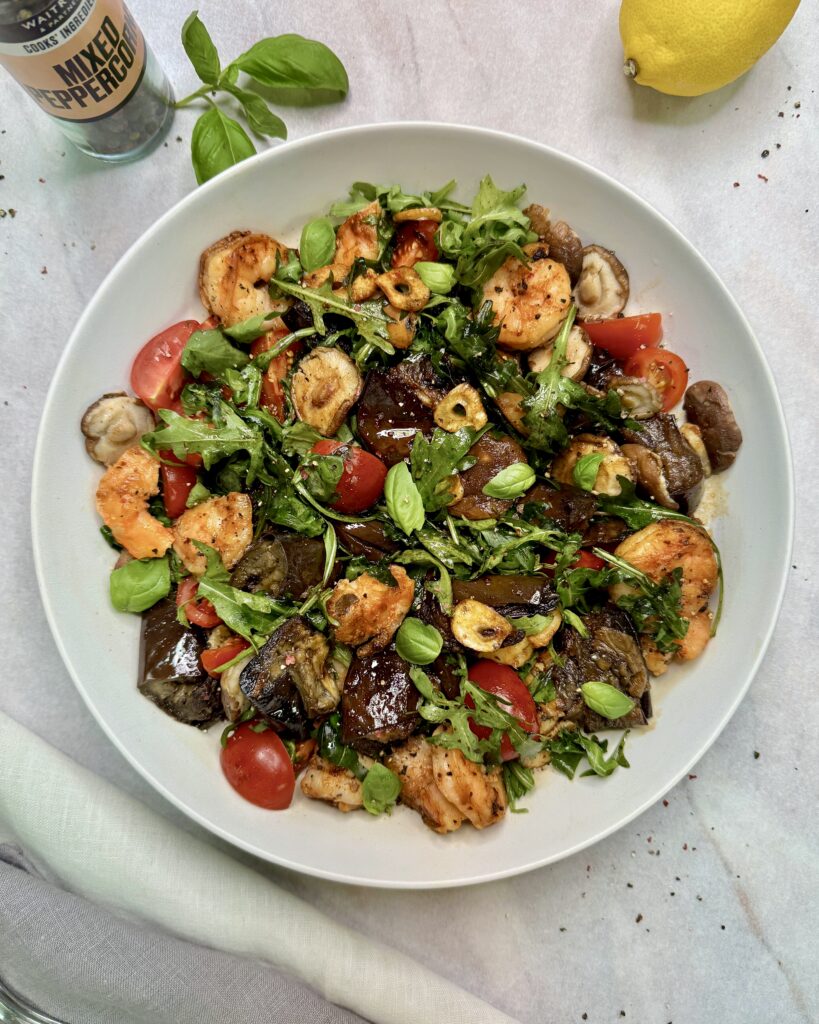 a plate with Prawn Salad with fried eggplant, shiitake mushrooms, garlic chips, tomatoes and greens