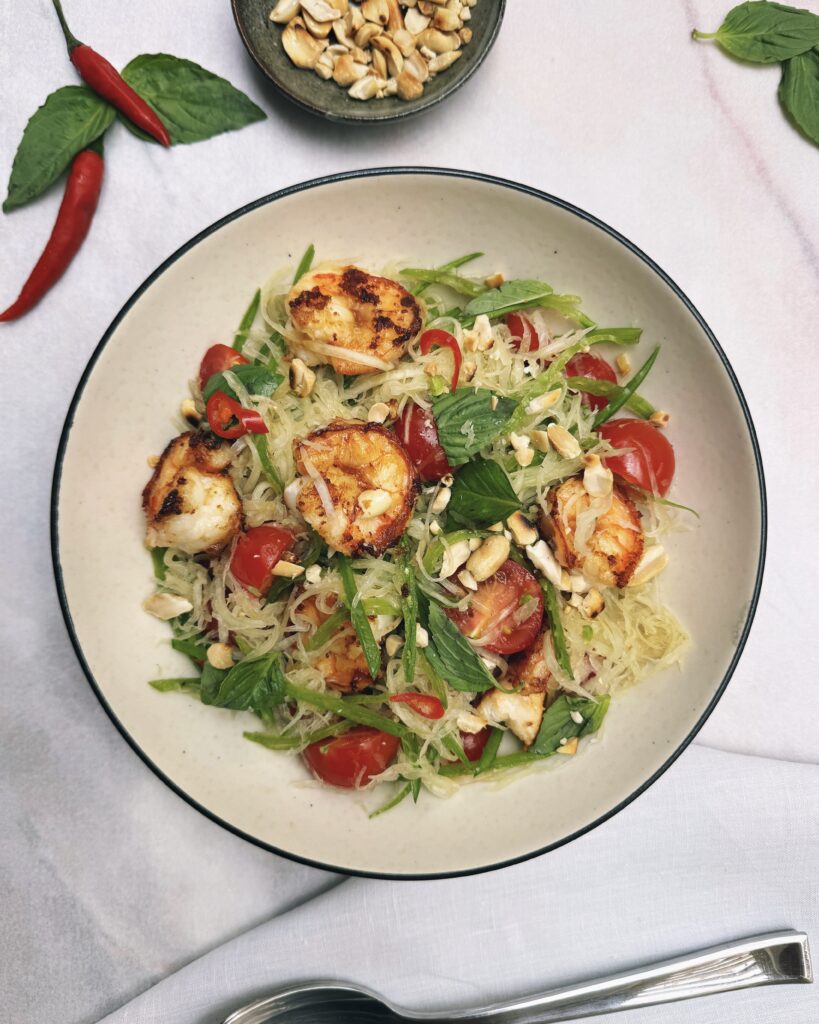 a salad plate with shredded green papaya, thai basil, snow peas, cherry tomatoes and prawns