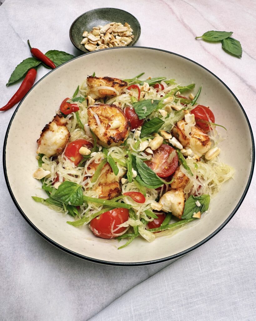 a salad plate with shredded green papaya, thai basil, snow peas, cherry tomatoes and prawns