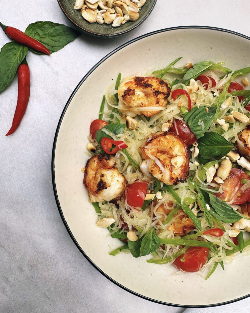 a salad plate with shredded green papaya, thai basil, snow peas, cherry tomatoes and prawns